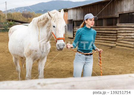 Horse breeder leading white horse through paddock 139251754