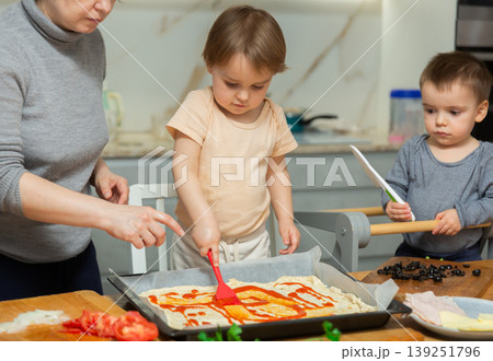 Mother and two young boys making pizza together in home kitchen Mother and two young boys making pizza together in home kitchen 139251796