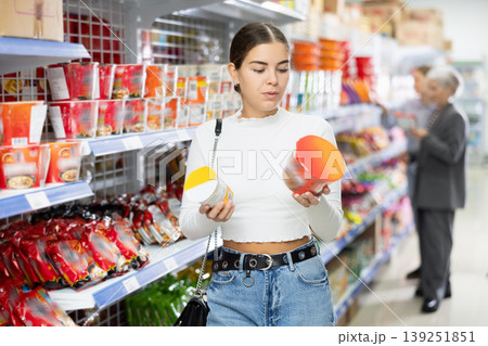 Young girl reading labels on cups of Asian instant noodles in store Young girl reading labels on cups of Asian instant noodles in store 139251851