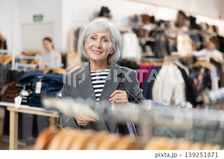 Old woman watching excitedly large stock of clothes in clothing store 139251871