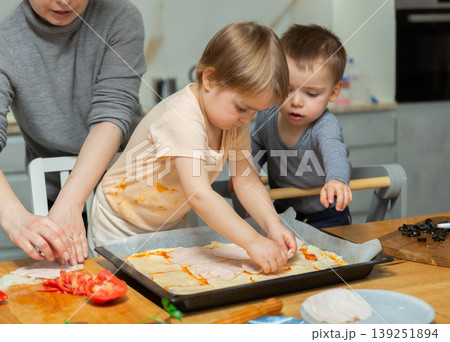 Family are cooking pizza together in cozy home kitchen. Cute kids with happy mother are preparing food or meal for dinner 139251894