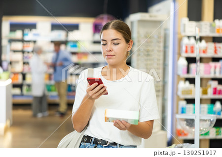 Woman scanning barcode on cosmetics package with her phone in pharmacy. Searching for information via Internet Woman scanning barcode on cosmetics package with her phone in pharmacy. Searching for information via Internet 139251917