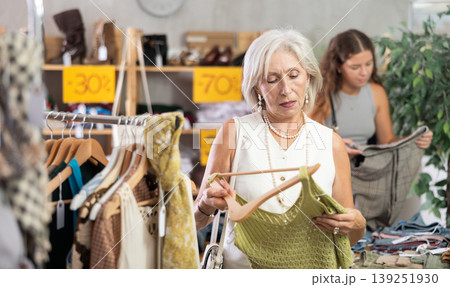 Elderly woman chooses top in clothing store Elderly woman chooses top in clothing store 139251930
