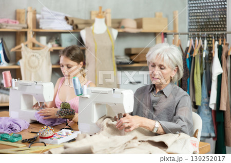 Two female dressmakers working with sewing-machine in tailor's workshop Two female dressmakers working with sewing-machine in tailor's workshop 139252017