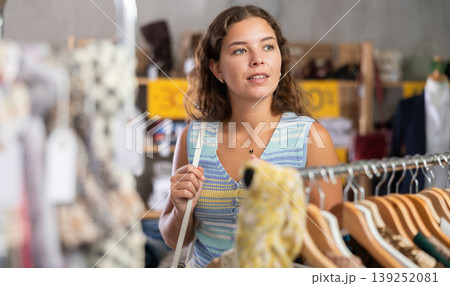 Young woman chooses a set of clothes for the summer. Visitor to the boutique examines new summer collection of clothes 139252081