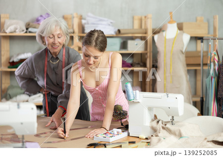 Elderly woman seamstress teaches young woman to draw pattern on paper 139252085