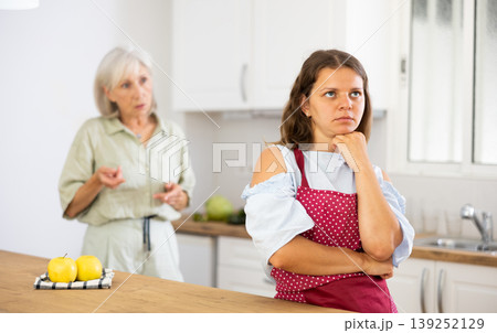 Senior woman scolding her adult daughter cooking breakfast in modern kitchen Senior woman scolding her adult daughter cooking breakfast in modern kitchen 139252129