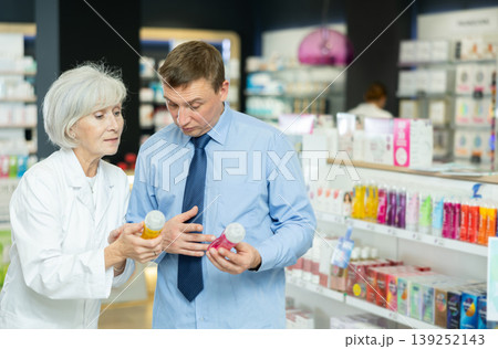 Senior woman pharmacist helps man buyer to decide on choice of lubricant. Senior woman pharmacist helps man buyer to decide on choice of lubricant. 139252143