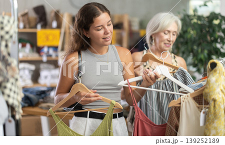 Two happy women of different ages choose summer clothes in fashion boutique Two happy women of different ages choose summer clothes in fashion boutique 139252189
