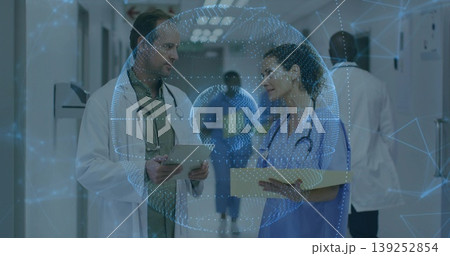 Reviewing data on tablet, two doctors in coats and scrubs walking hospital corridor with sanitizer Reviewing data on tablet, two doctors in coats and scrubs walking hospital corridor with sanitizer 139252854