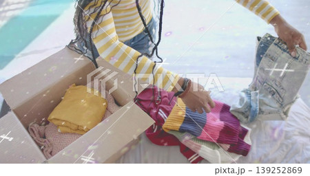 Woman wearing yellow striped top sorting and packing sweater in home bedroom, with cardboard box Woman wearing yellow striped top sorting and packing sweater in home bedroom, with cardboard box 139252869