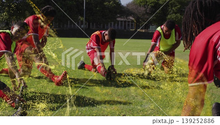 Stretching seven soccer players wearing red jerseys and colored bibs on grass field, with ball 139252886