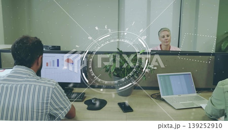 Displaying bar and pie charts on desktop monitor beside green potted plant on open-plan bench desk 139252910