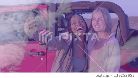 Taking selfie friends wearing sunglasses holding smartphone beside red off-road vehicle in desert 139252955