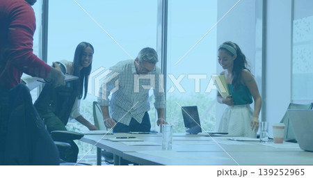 Leaning colleagues in formal attire reviewing documents on conference table, with laptop and tablet 139252965