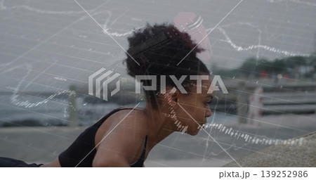 Doing pushups woman in sportswear on ledge by sea with earbuds, financial overlay, copy space Doing pushups woman in sportswear on ledge by sea with earbuds, financial overlay, copy space 139252986