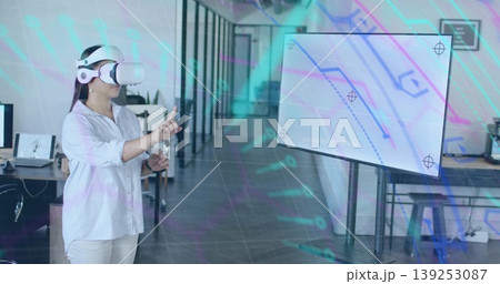 Pointing Asian woman wearing VR headset selecting virtual elements in open-plan office, copy space Pointing Asian woman wearing VR headset selecting virtual elements in open-plan office, copy space 139253087
