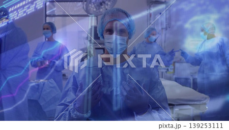Central surgeon adjusting blue gown mask cap and gloves in operating room, with data overlays 139253111