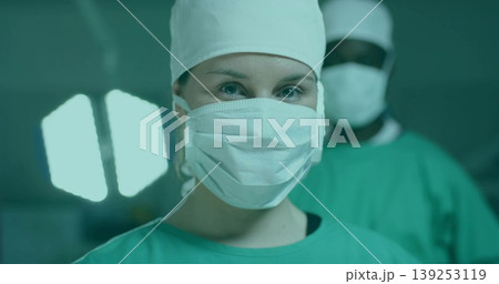 Operating female surgeon in green scrubs and mask performing surgery in hospital OR, with OR lamp Operating female surgeon in green scrubs and mask performing surgery in hospital OR, with OR lamp 139253119