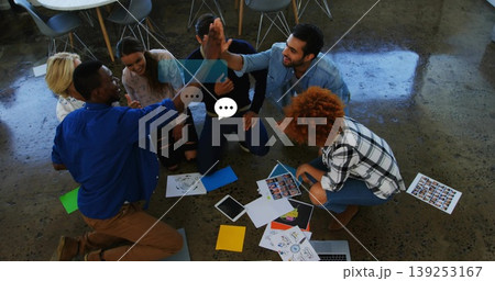 High-fiving six coworkers kneeling on office floor, with sheets, sticky notes, charts and devices High-fiving six coworkers kneeling on office floor, with sheets, sticky notes, charts and devices 139253167