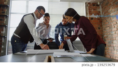 Reviewing business casual professionals leaning over plans at loft office, with laptop and tablet Reviewing business casual professionals leaning over plans at loft office, with laptop and tablet 139253679