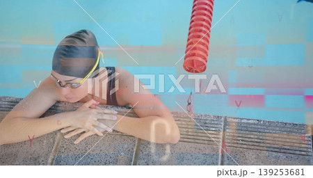 Resting swimmer wearing swim cap and goggles at pool edge, with red lane floats, turquoise water Resting swimmer wearing swim cap and goggles at pool edge, with red lane floats, turquoise water 139253681