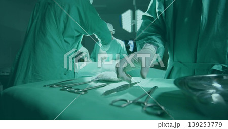 Reaching gloved surgeon's hand selecting scalpel on draped tray under lights in operating room Reaching gloved surgeon's hand selecting scalpel on draped tray under lights in operating room 139253779