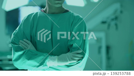 Standing Indian surgeon crossing arms in operating room, with green scrubs gloves lights equipment Standing Indian surgeon crossing arms in operating room, with green scrubs gloves lights equipment 139253788