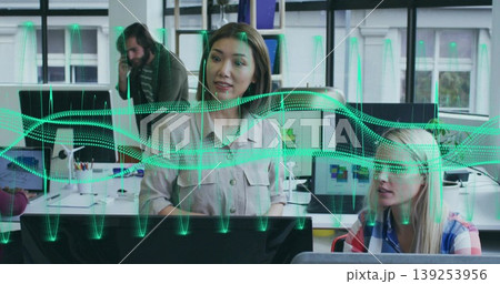 Presenting Asian woman showing real time data on monitors in shared office, with green overlay 139253956