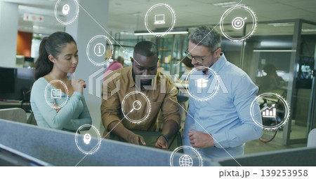 Pointing at keyboard three colleagues discussing project at cubicle desk in office, with data icons Pointing at keyboard three colleagues discussing project at cubicle desk in office, with data icons 139253958