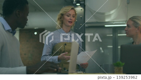 Presenting White woman in office attire showing charts in meeting area, with laptops, coffee mug 139253962