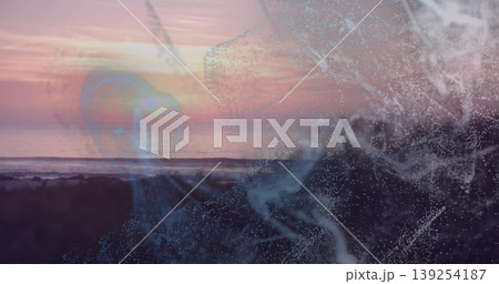 Glowing abstract digital particle swirl drifting across rocky shoreline, with ocean horizon overlay 139254187
