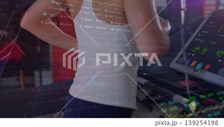 Running mid adult woman monitoring stock charts and tickers inside home gym, with treadmill console Running mid adult woman monitoring stock charts and tickers inside home gym, with treadmill console 139254198