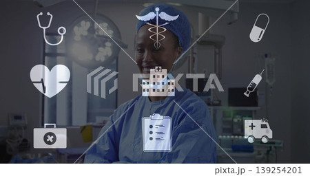 Smiling Black surgeon in scrubs crossing arms under surgical light in OR with medical icon overlay Smiling Black surgeon in scrubs crossing arms under surgical light in OR with medical icon overlay 139254201