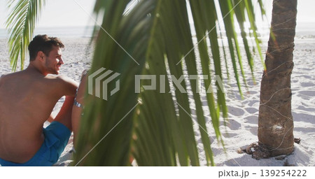 Leaning man toward woman in bikini on beach with palm frond facing ocean horizon, copy space Leaning man toward woman in bikini on beach with palm frond facing ocean horizon, copy space 139254222
