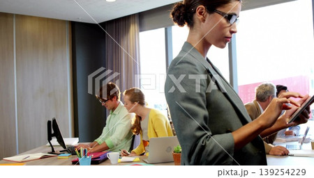 Standing woman in gray blazer using tablet in meeting room with laptops potted plant, copy space Standing woman in gray blazer using tablet in meeting room with laptops potted plant, copy space 139254229