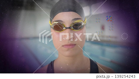 Focusing competitive swimmer standing at pool edge, with black swim cap and yellow-tinted goggles 139254243
