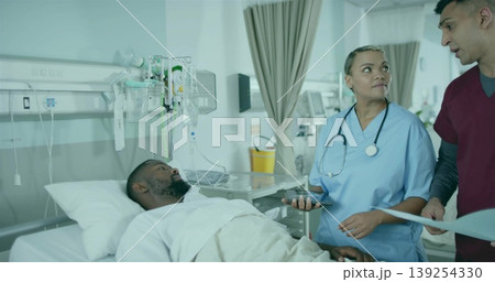 Supporting medical team caring for patient wearing gown reclining in bed, with IV stand and chart 139254330