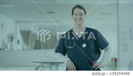 Smiling nurse in navy scrubs leaning on table in hospital corridor, with stethoscope, patient beds 139254346