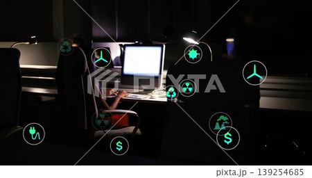 Pacific Islander woman in t-shirt typing at office PC at night, with floating energy finance icons 139254685