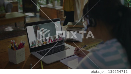 Taking notes, Asian girl wearing striped shirt, headset at home study desk, with laptop, copy space 139254711