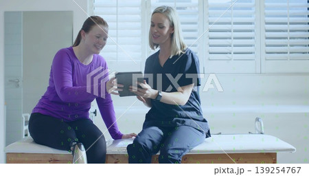 Sharing tablet content, clinician in scrubs, patient in workout wear on wooden exam table in clinic Sharing tablet content, clinician in scrubs, patient in workout wear on wooden exam table in clinic 139254767