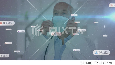 Senior doctor adjusting surgical mask in hospital corridor wearing stethoscope, with digital badges Senior doctor adjusting surgical mask in hospital corridor wearing stethoscope, with digital badges 139254776