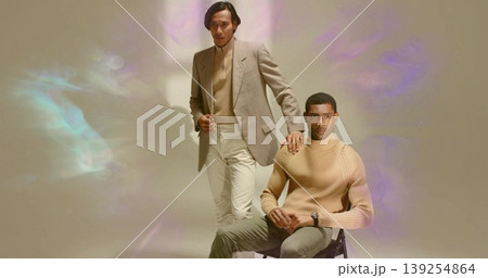 Posing male models wearing beige sweaters and blazer in fashion studio, featuring chair, wristwatch Posing male models wearing beige sweaters and blazer in fashion studio, featuring chair, wristwatch 139254864