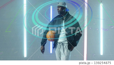 Posing male athlete in sportswear holding orange basketball in tech studio, with hologram rings 139254875
