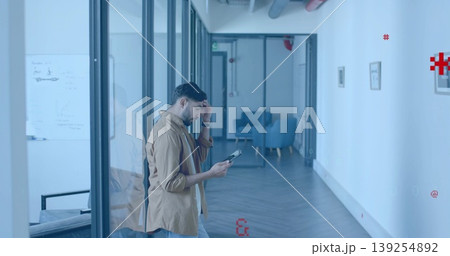 Walking Indian man wearing shirt and jeans holding tablet in glass corridor, with whiteboard Walking Indian man wearing shirt and jeans holding tablet in glass corridor, with whiteboard 139254892