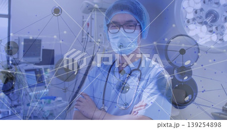Standing Chinese doctor in scrubs in OR with stethoscope, monitor and pump under digital overlay 139254898