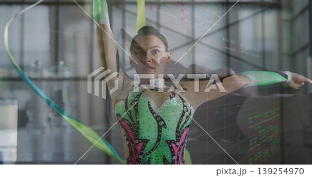 Performing female gymnast swirling ribbon in sports hall, with glittering leotard and sleeves Performing female gymnast swirling ribbon in sports hall, with glittering leotard and sleeves 139254970