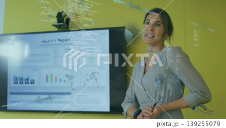 Presenting consultant in dress pointing to glass board in meeting, with monitor, stylus, copy space 139255079
