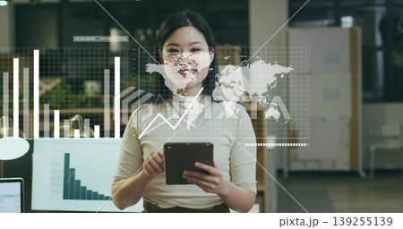 Data analyst woman wearing beige and brown outfit reviewing 3D charts at office desk, with tablet 139255139